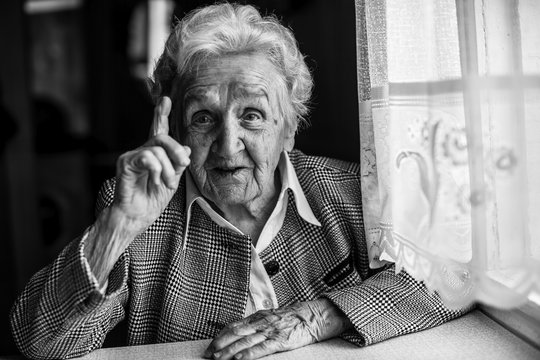 Elderly women gesticulating when speaking, sitting near the window. Black-and-white portrait.