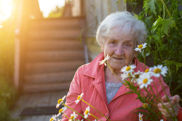 Elderly woman near village houses, portrait with daisies.
