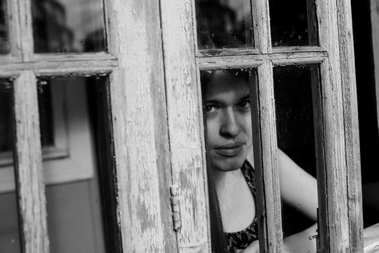 Young woman looking through window, black-and-white photography.