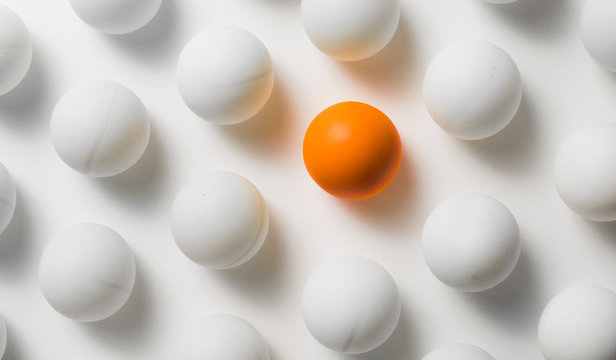 Orange ping pong balls surrounded with white balls one white background .