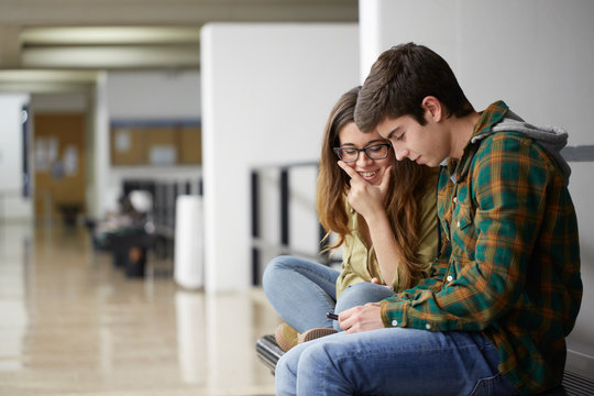 Young couple of students using a phone in the hall of the university