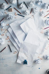 Blank paper on a wooden background with inkwell and scattered crumpled paper balls, pencils and...