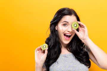  Happy young woman holding kiwis on a yellow background