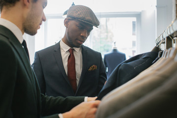 Men's Fashion Shopping - Caucasian Shop Assistant Showing Suits to Young Black Customer