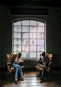 Multi-ethnic couple by the window in two armchairs talking to each other
