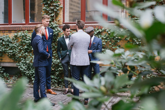 Group of Five Well-Dressed Young Men in Suits Standing in Courtyard