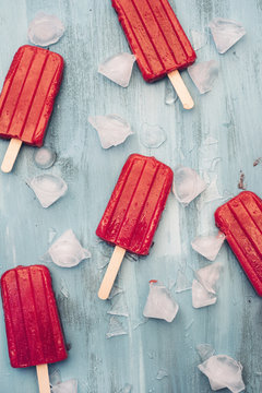 Food: Homemade strawberry popsicles on blue background with ice cubes