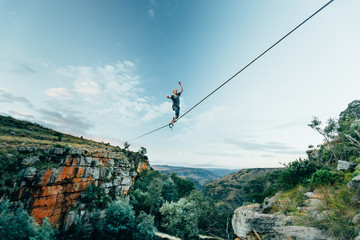 Man tightrope walking a high line over a lush gorge in the mountains