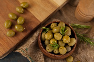 Olives with rosemary in bowl by cutting board