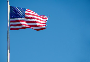 American flag on pole with frayed edge on bright blue sky background