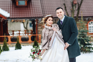 Fototapeta premium Winter wedding outdoors on background of snow-covered house. Bride and groom are standing and hugging.