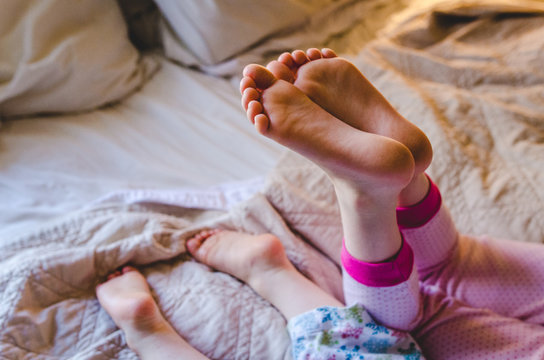 Bare feet of two kids lying on a bed in their pajamas