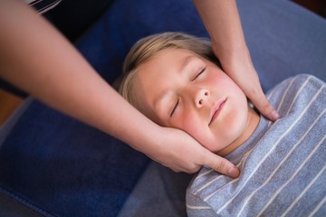 Boy lying with eyes closed receiving neck massage from female