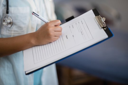 Midsection Of Female Doctor Writing On Clipboard