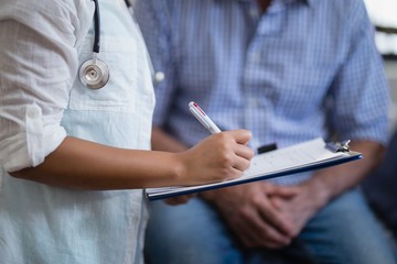 Midsection of female therapist writing on clipboard with male
