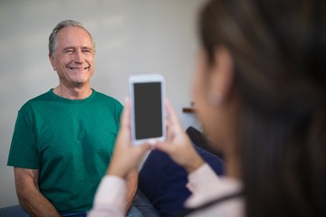 Female therapist photographing senior male patient from mobile