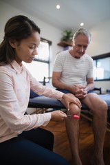 Female therapist examining knee of senior male patient with