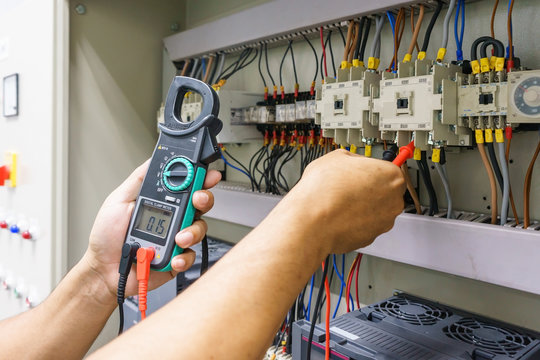 Electrical Engineer adjusts electrical equipment with a multimeter tester in his hand closeup. Professional electrician in electric automation cabinet