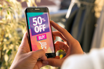 Girl holding a smartphone with a 50% discount advertising on the screen. Marketing, ecommerce, cell phone publicity.