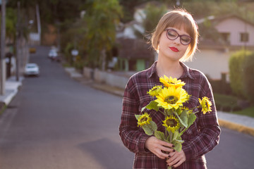Fototapeta premium Blodne young woman holding sunflowers by the sunset