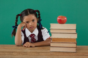 Schoolgirl sitting beside books stack with apple on top against
