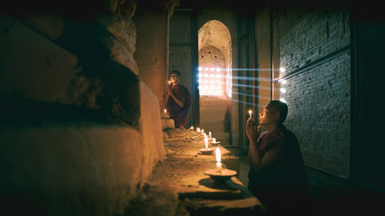 Novices praying with candles in front of buddha statue inside old pagoda, Bagan Myanmar