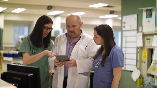 Nurses and doctor collaborate on a tablet computer in hospital.