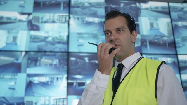  Security officer watching CCTV video screens & talking on radio