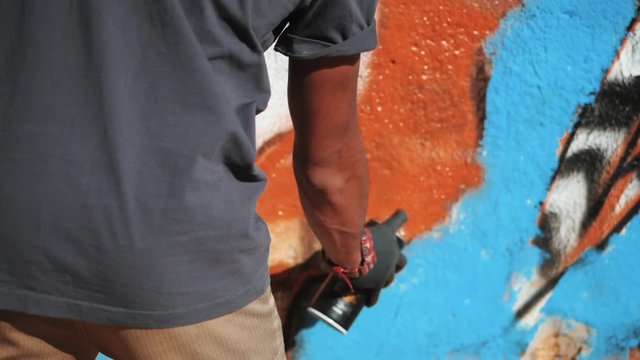 Graffiti Artist Painting On The Street Wall. Male hand with aerosol spray bottle spraying with colorful paint, Urban Outdoors Art Concept. Slow motion. Close up view