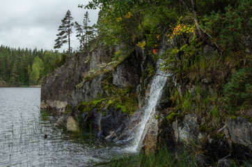 A small waterfall flows into the lake from a rocky shore. Ladoga lake. Karelia. Russia.