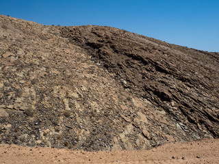 Closeup scene of rough rock mountain texture pattern view with clear blue sky background on unpaved dirt road
