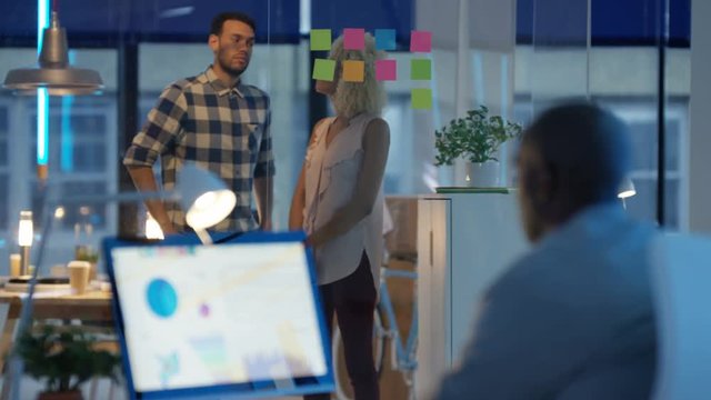 Casual business team in modern office working on computer and brainstorming with sticky notes .
