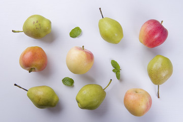 Fresh fruits: apples and pear with mint leaves on a white table.