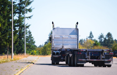 Big rig semi truck with flat bed trailer turn on road with trees