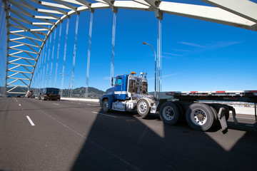 Fototapeta na wymiar Big rig semi truck with long flat bed trailer running on arched truss bridge