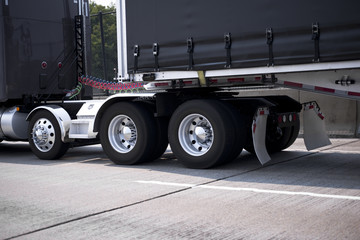 Black big rig semi truck with chrome wheels and fenders and black tented frame semi trailer going by roadway