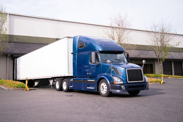Dark blue big rig semi truck with trailer in warehouse dock loading commercial cargo