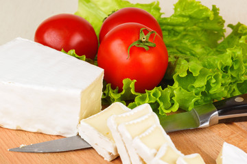 Cheese slices, tomatoes and lettuce leaf for breakfast on a wooden cutting board.