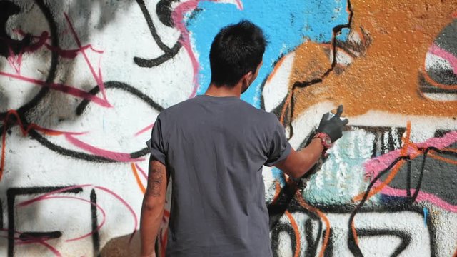 Handsome Talented Young Boy making a colorful graffiti with aerosol spray on urban street wall. Cinematic toned slow motion footage. Creative art.