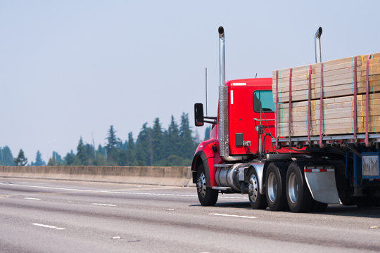 Red big rig semi truck transport timber on flat bed semi trailer