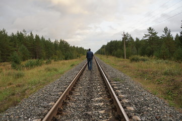 A young man walks along the rails in the forest zone. View from the back