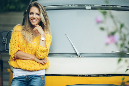 Happy smiling woman is wearing yellow sweater near old retro bus