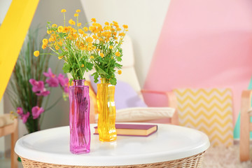 Vases with bouquets of beautiful flowers on table in room