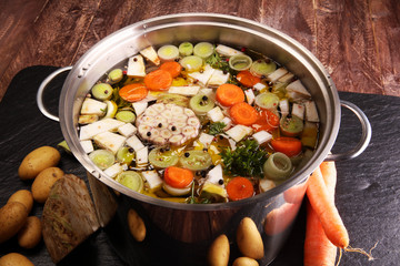 Broth with carrots, onions various fresh vegetables in a pot - colorful fresh clear spring soup. Rural kitchen scenery vegetarian bouillon or stock