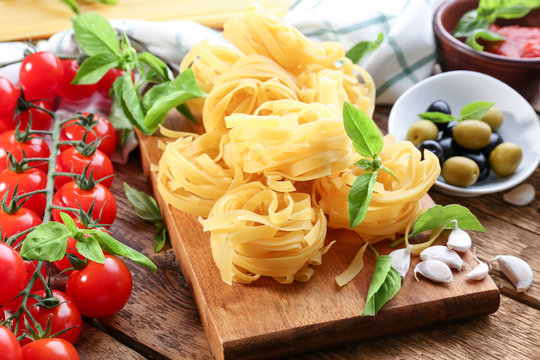 Pasta nests, tomatoes and olives on wooden table