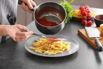 Woman adding tasty tomato sauce to pasta on plate