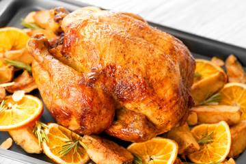 Roasted turkey with slices of orange and potatoes on baking sheet