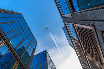 Fototapeta na wymiar Tall city buildings and a plane flying overhead.