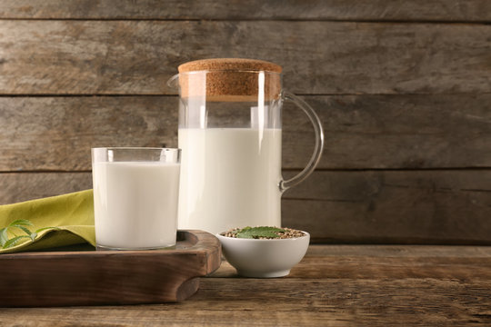 Glass and jug with hemp milk on wooden background