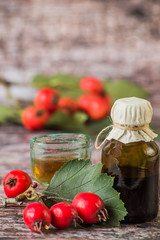     Tincture of hawthorn in a small glass bottle and fresh hawthorn fruit with leaves on a wooden background. Used in folk and traditional medicine.